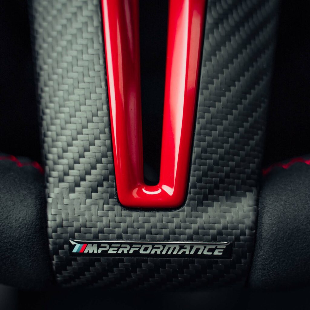 A close up shot of a dry carbon bmw m performance steering wheel trim with the M performance logo and red painted inner piece
