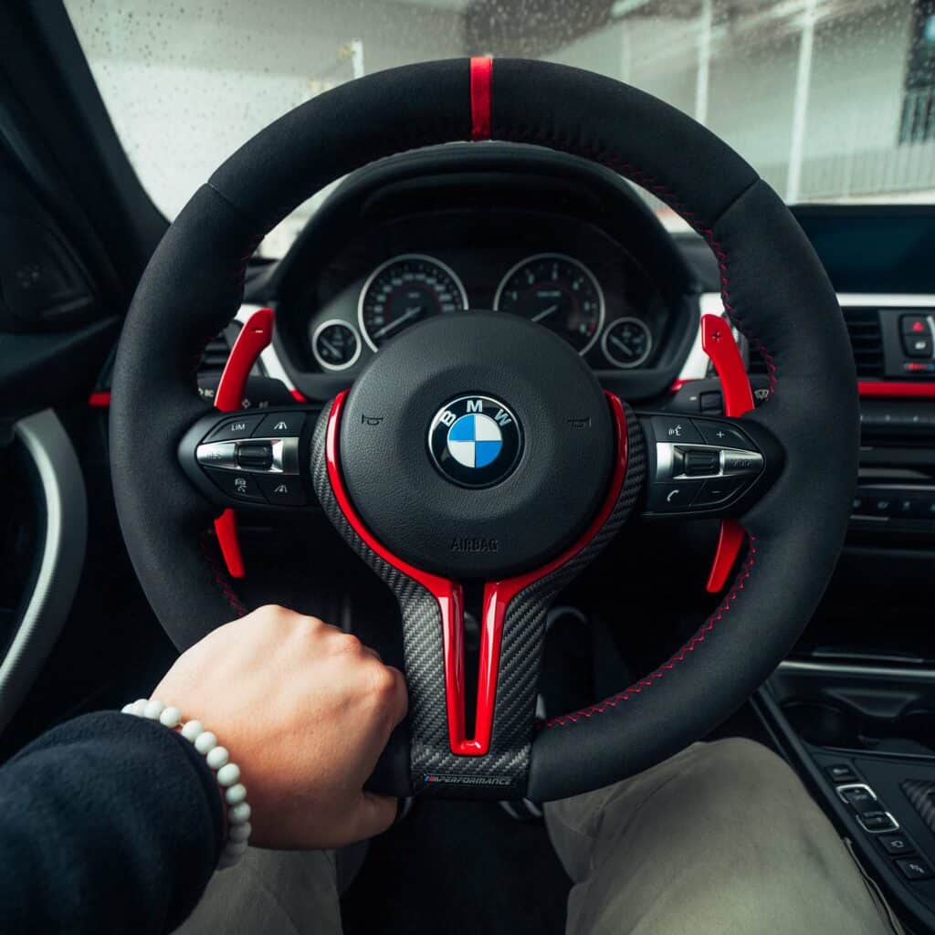 man holding an alcantara steering wheel with red stitching and red 12 o'clock striping with red aluminium paddle shifters and carbon steering wheel tirm